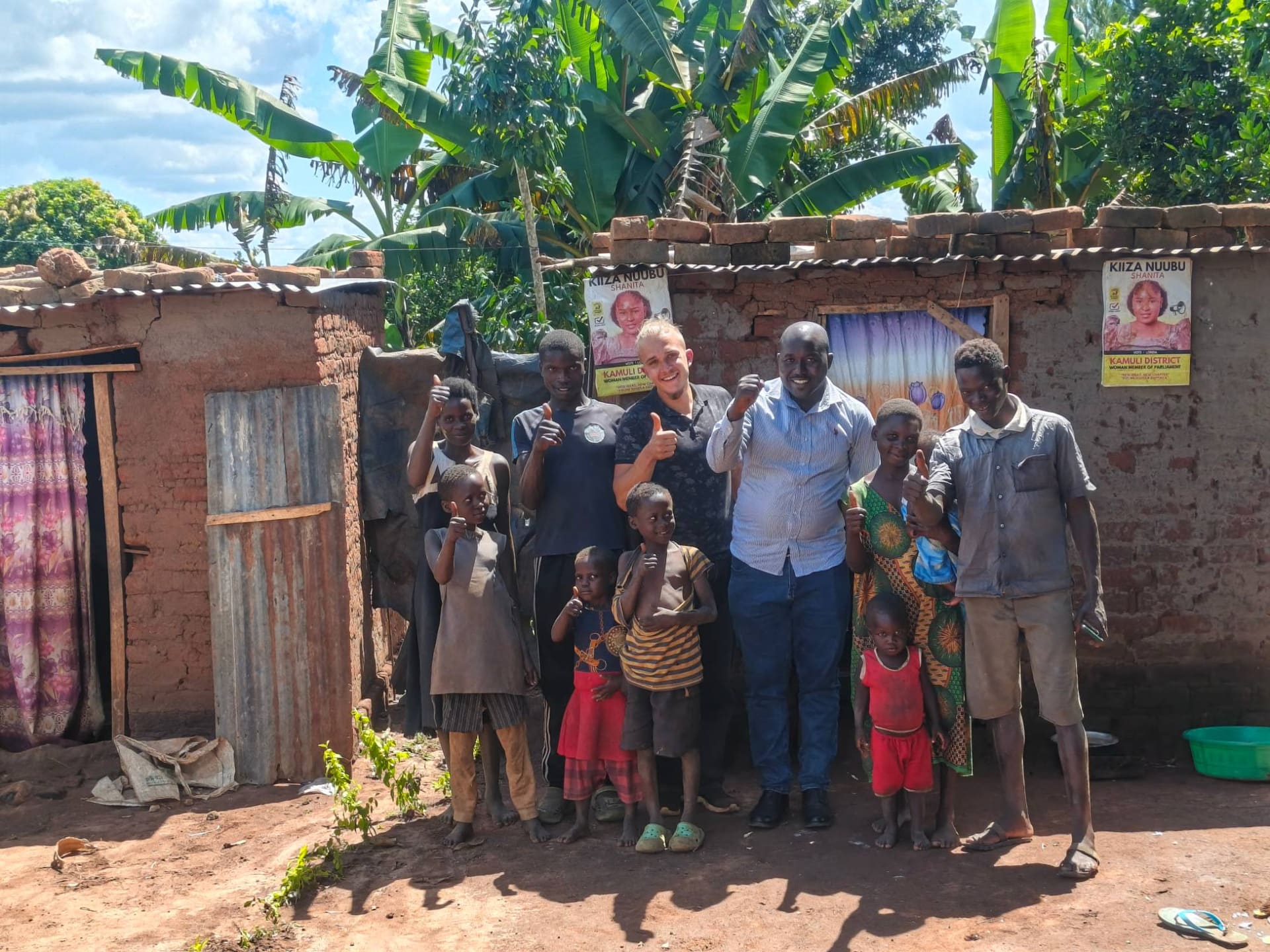 Projektteam mit einer Familie vor ihrem Haus in der Region Kamuli